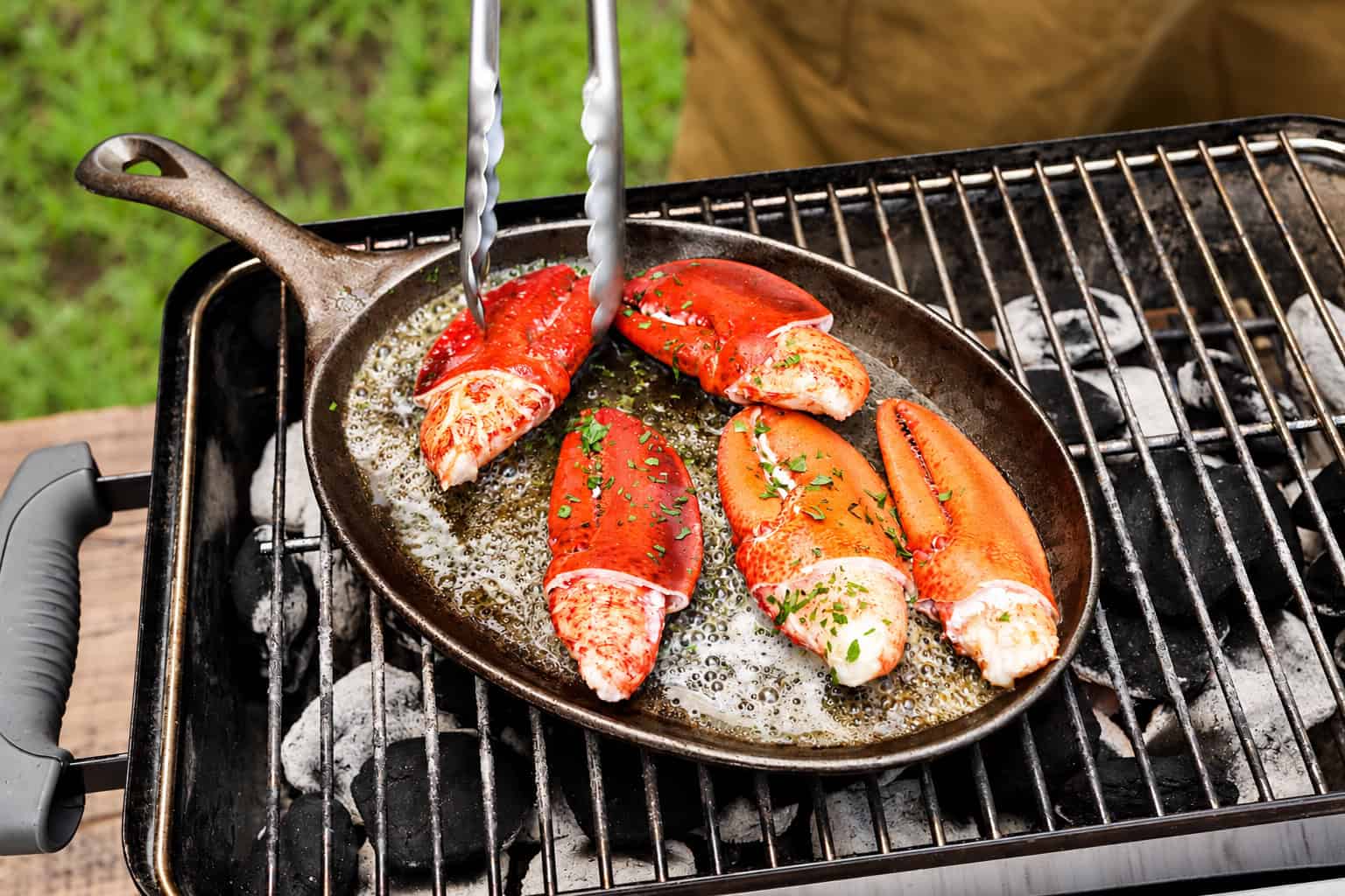 Cooked lobster claws warming in butter in a cast-iron skillet on a grill