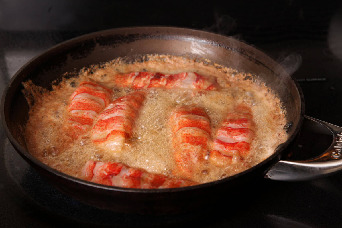 Shucked lobster tail meat cooking in butter in a skillet