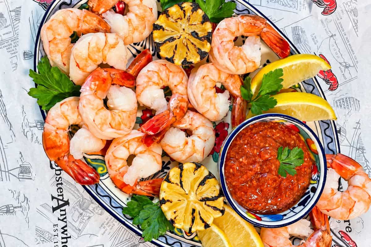 Cooked shrimp on a platter with lemon, parsley, and cocktail sauce